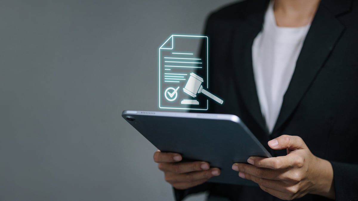 Business person holding a tablet with a virtual legal document icon featuring a gavel and checkmark. Concept of digital contracts, e-signatures, court verdicts, and lawtech.